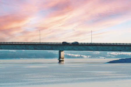 Highway bridge with traffic driving on it, spanning across a frozen bay on a winters evening. High...