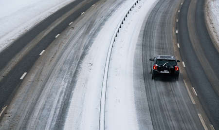 Cars driving on a highway in a blizzard with the road covered in snow and ice on a cold winters day....