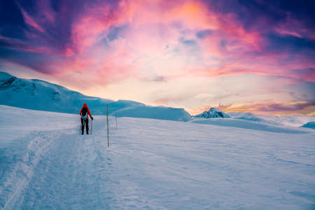 Person walking on a mountain trail in the snow in a majestic artic wilderness during sunset. High...