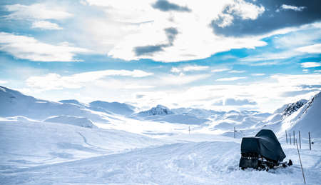 Snowmobile parked by a trail in the snow leading to a wild mountain range in winter. High quality photoの写真素材