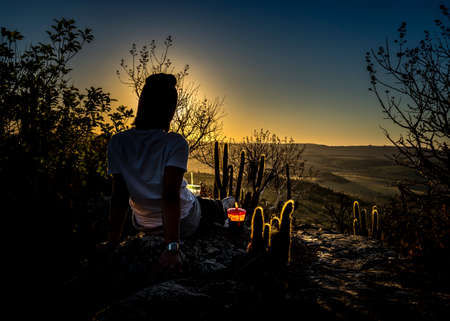 girl contemplating the sunset on mountain peak surrounded by cactiの写真素材