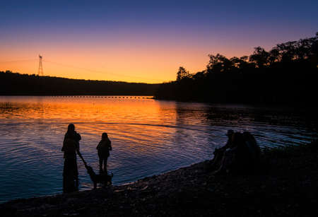 people playing with dog by the water at duskの写真素材