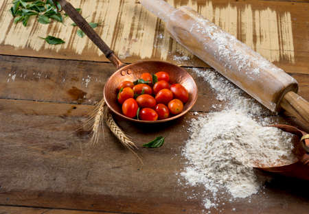 cherry tomatoes in small copper pot, rolling pin, basil leaves and flour on the wooden.の写真素材