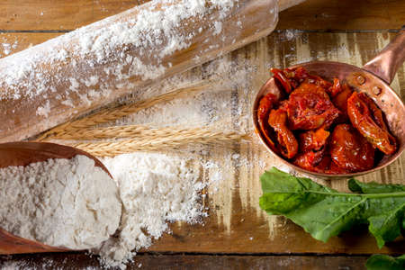 dried tomatoes in small copper pot, rolling pin, rocket leaves and flour on the wooden table.の写真素材