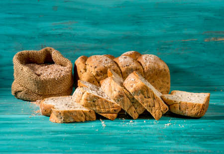 sliced whole bread and small bag with whole wheat flour on textured blue wood