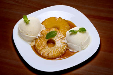 slice of roasted pineapple, caramelized on white plate with 2 scoops of vanilla ice creamの写真素材