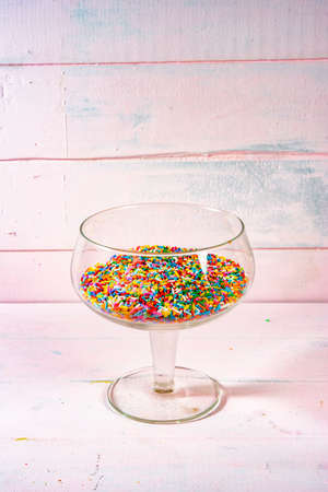colourful candy and sprinkles in transparent bowl on light pink wood backgroundの写真素材