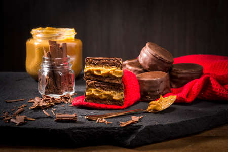 alfajores with dulce de leche, pot and spoon of milk sweet and chocolate shavings on the red clothの写真素材