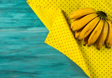 bananas on yellow fabric with fold over blue wooden background, top viewの写真素材