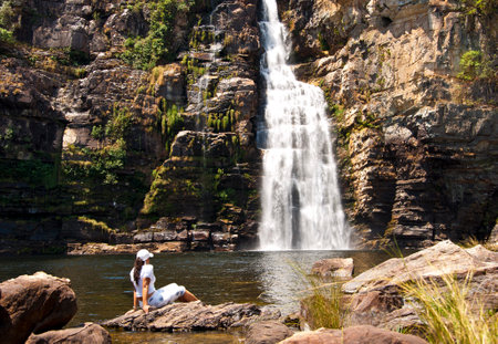 Young couple sitting on the rocks and looking at the waterfall in the background, Chapada dos...