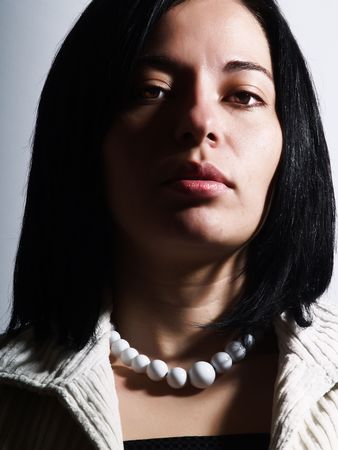 A high-key portrait about an attractive lady with black hair who is looking ahead and she has a glamorous look. She is wearing a white coat, a black dress and a white necklace.の写真素材