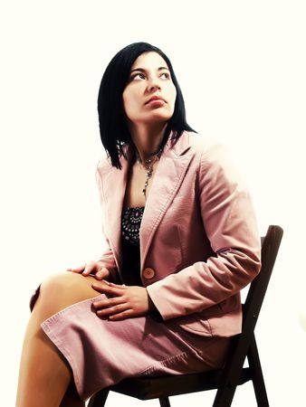 A portrait about an elegant trendy lady with black hair who is sitting on a chair and she is looking up. She is wearing a nice dress, a pink skirt and a pink stylish coat.の写真素材