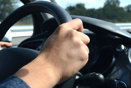 Right hand holding the wheel while driving on road
