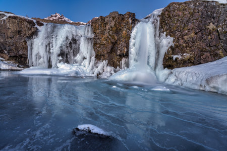 Frozen Kirkjufellfoss or Kirkjufell waterfall during a beautiful sunrise covered in snow and ice in Icelandの写真素材