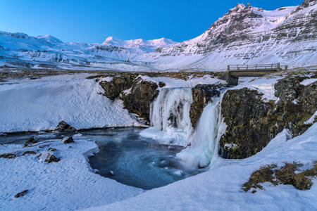 Frozen Kirkjufellfoss or Kirkjufell waterfall during a beautiful sunrise covered in snow and ice in Icelandの写真素材