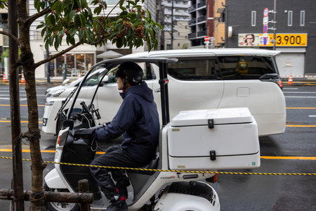 Tokyo, Japan, October 29, 2023: Delivery personnel on electric vehicle at city intersectionのeditorial素材