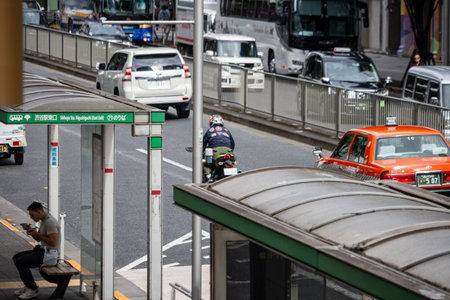 Tokyo, Japan, October 29, 2023: Man sitting at bus stop with traffic in the backgroundのeditorial素材