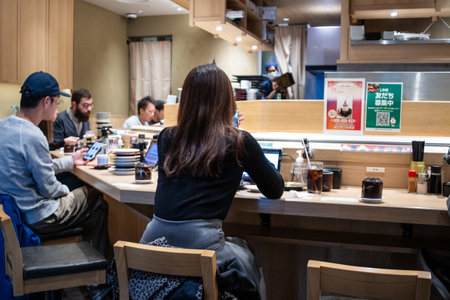Tokyo, Japan, October 29, 2023: Diners seated at a sushi bar with a chef preparing mealsのeditorial素材