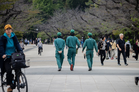 Tokyo, Japan, October 31, 2023: Group of workers in green uniforms walking in a park with pedestriansのeditorial素材