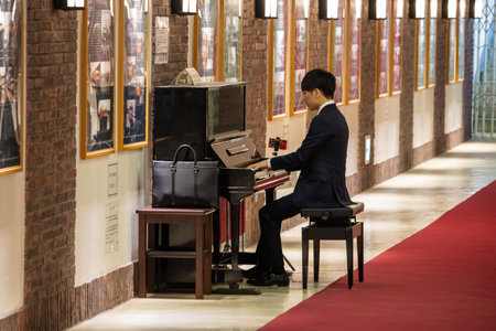 Tokyo, Japan, November 1, 2023: Man Playing Piano in a Hallway with Framed Picturesのeditorial素材