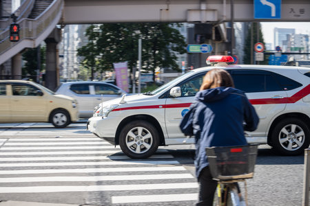 Tokyo, Japan, November 1, 2023: Cyclist Waiting at Pedestrian Crossing with Police Car in Backgroundのeditorial素材