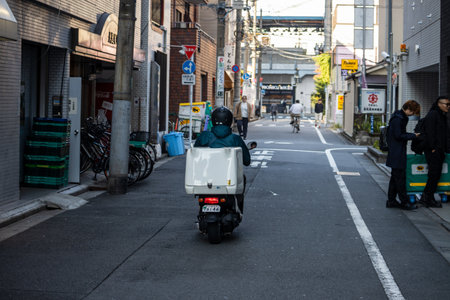 Tokyo, Japan, November 1, 2023: Delivery Person on Scooter in Alleywayのeditorial素材