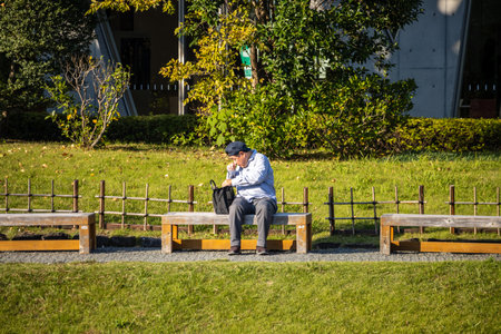 Tokyo, Japan, November 1, 2023: Man sitting alone on a park benchのeditorial素材