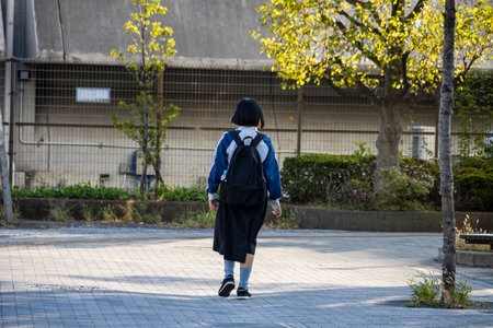 Tokyo, Japan, November 1, 2023: Lone student walking on an urban sidewalk with trees and modern architectureのeditorial素材