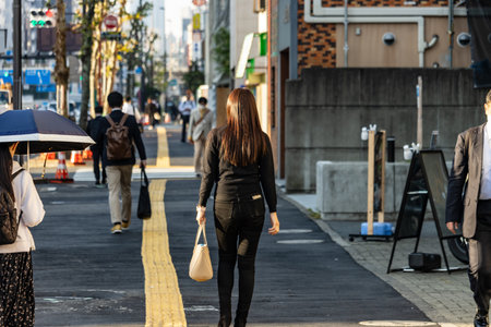 Tokyo, Japan, November 2, 2023: Pedestrians walking on a sunny Tokyo street with umbrellas and business attractionsのeditorial素材