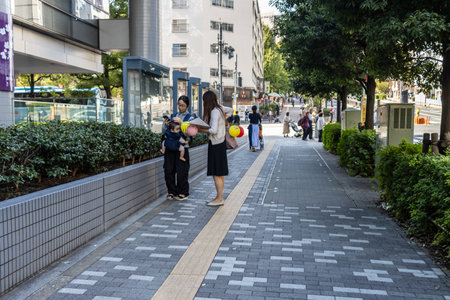 Tokyo, Japan, November 2, 2023: Woman and Child on Sidewalk with Balloons and Urban Backdropのeditorial素材