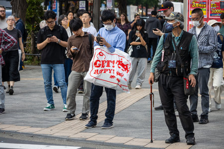 Tokyo, Japan, November 2, 2023: Crowd Walking in a Commercial Area with Man Holding "Get Happy" Signのeditorial素材
