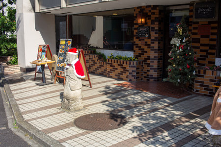 Tokyo, Japan, November 4, 2023: Traditional Stone Statue Decorated in Santa Hat Outside a Local Restaurantのeditorial素材