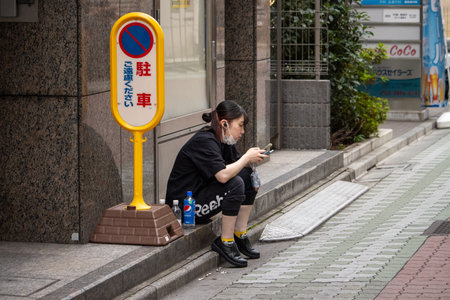 Tokyo, Japan, November 5 2023: Young woman using smartphone while sitting on sidewalkのeditorial素材