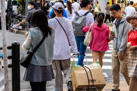 Tokyo, Japan, November 6, 2023: Pedestrians with smartphones and shopping bags crossing street