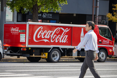Tokyo, Japan, November 7, 2024: Coca-Cola Delivery Truck on the Street with Passing Businessmanのeditorial素材