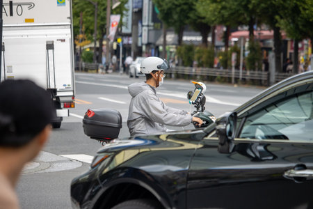 Tokyo, Japan, November 7, 2024: Delivery Man on Scooter with Mobile Phone Holder