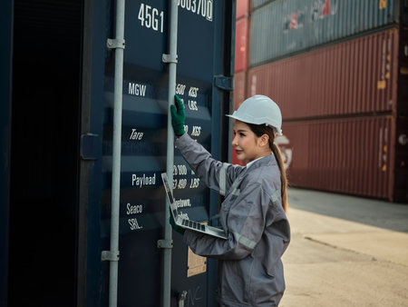 portrait of young asian woman wearing safety helmet and working with container box at shipping yard