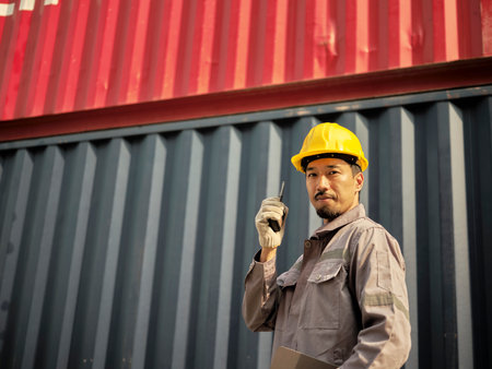Asian worker wearing safety helmet and using walkie talkie in front of container cargo freight ship for Logistic Import Export background.の写真素材