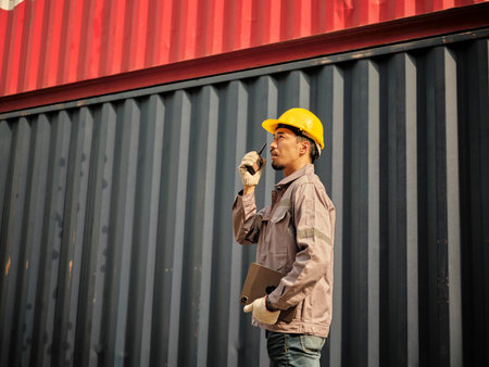 Asian worker wearing safety helmet and using walkie talkie communicate with the lifting container team in front of container cargo freight ship for Logistic Import Export background.の写真素材