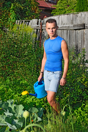 A young man with a blue watering can around the garden with cabbage on the farm in summer Sunny dayの写真素材