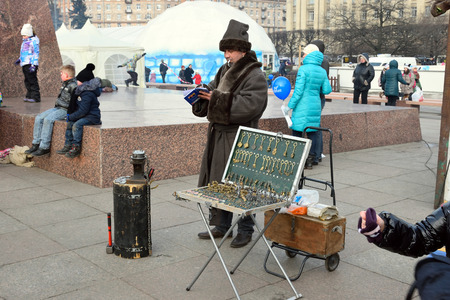 ST.PETERSBURG, RUSSIA - MARCH 13, 2016: The blacksmith is the master of making coins in an old coat next to the anvil and finished gifts on the holiday of Maslenitsa at Moscow squareのeditorial素材