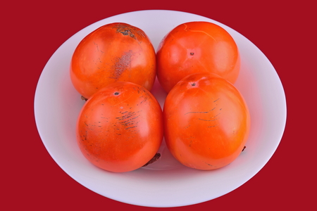 Persimmon fruit on a white plate on a red background.の写真素材