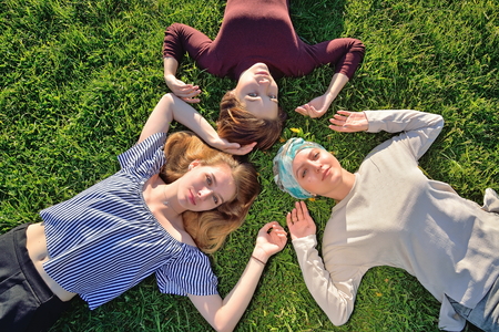 Three young girls lying on green lawn in summer.の写真素材