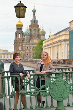 Young girls are on Italian bridge across the Griboyedov Canal in front of the Cathedral of the Savior on Blood in Saint-Petersburgの写真素材