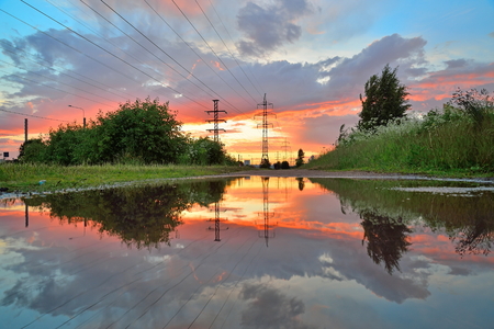 High-power line - power lines are reflected in a puddle after the rain at sunsetの写真素材