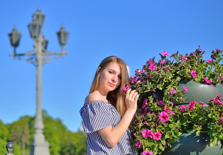 Beautiful girl standing near flower bed in front of an ancient street lampの写真素材