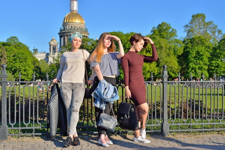 Three young girls thoughtfully standing at the iron fence on the background of St. Isaac's Cathedral in Saint-Petersburg.の写真素材