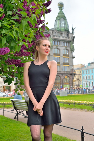 Beautiful girl looks into the distance from the Bush lilac lilac against the House of the book - singer in Saint-Petersburgの写真素材
