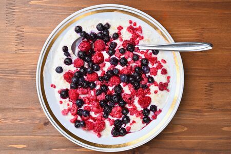 Oatmeal porridge in a bowl of ice cream raspberries and blueberries on a brown wooden table.の写真素材