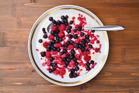 Oatmeal porridge in a bowl of ice cream raspberries and blueberries on a brown wooden table.の写真素材
